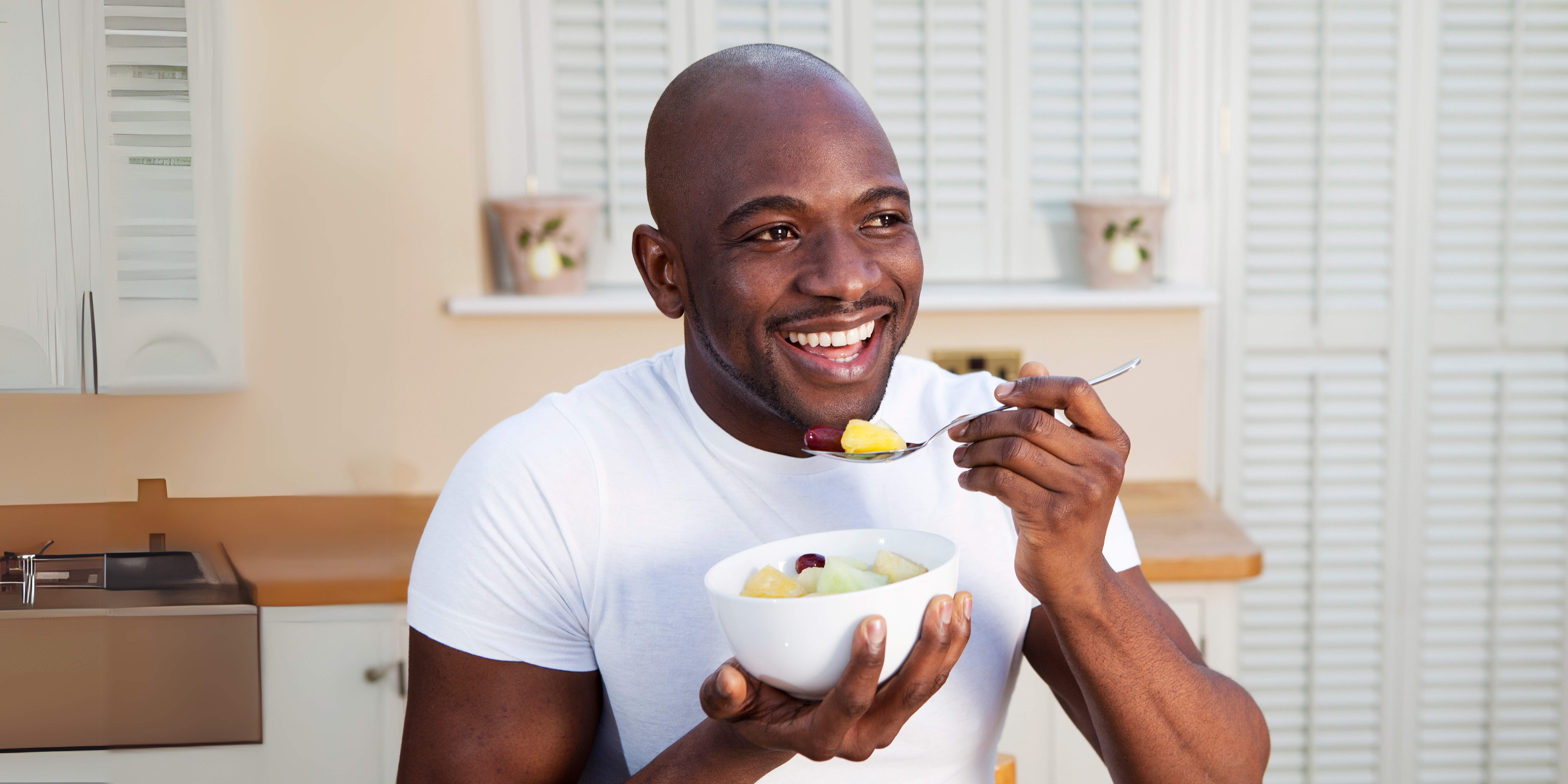 Man in white t-shirt eating fresh fruit and smiling, happy to have a healthy relationship with food while taking GLP-1